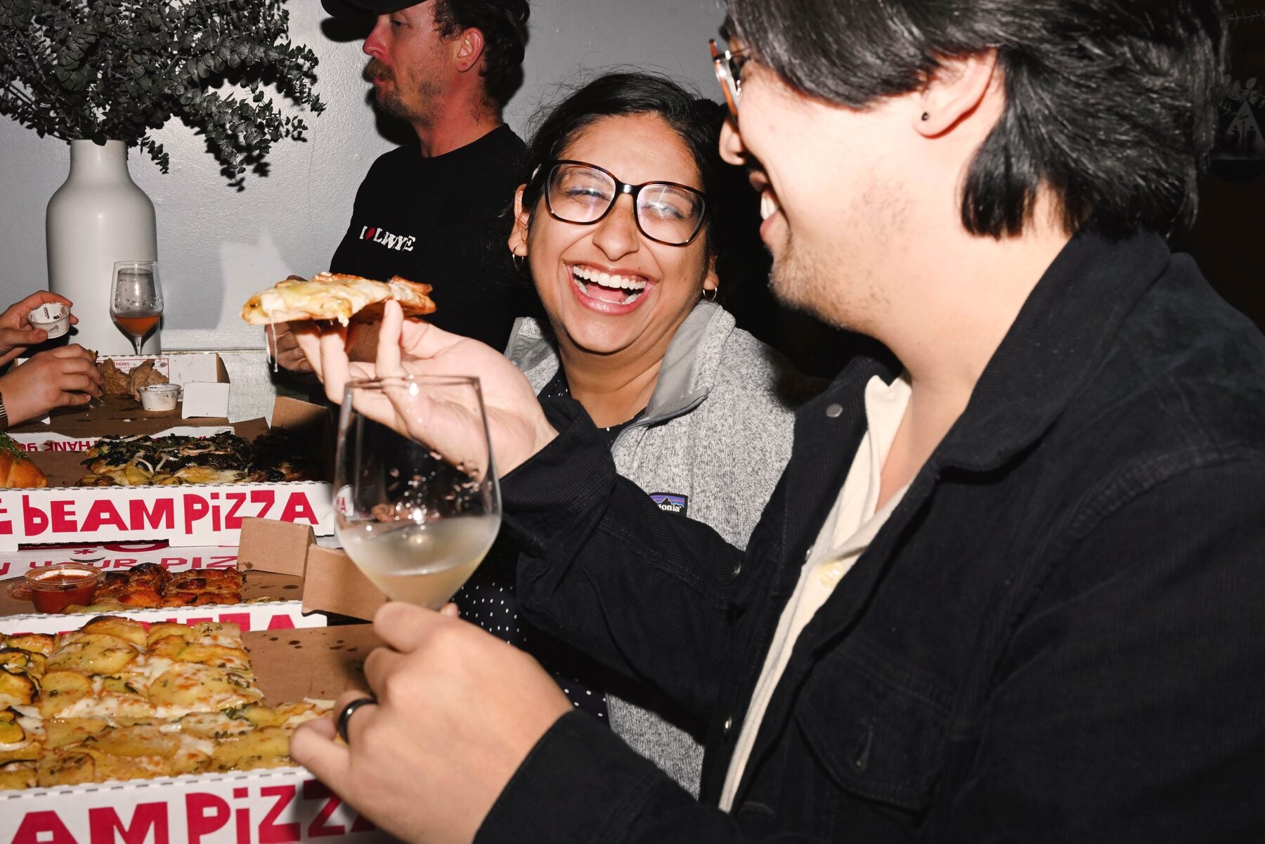Friends laughing over wine and pizza